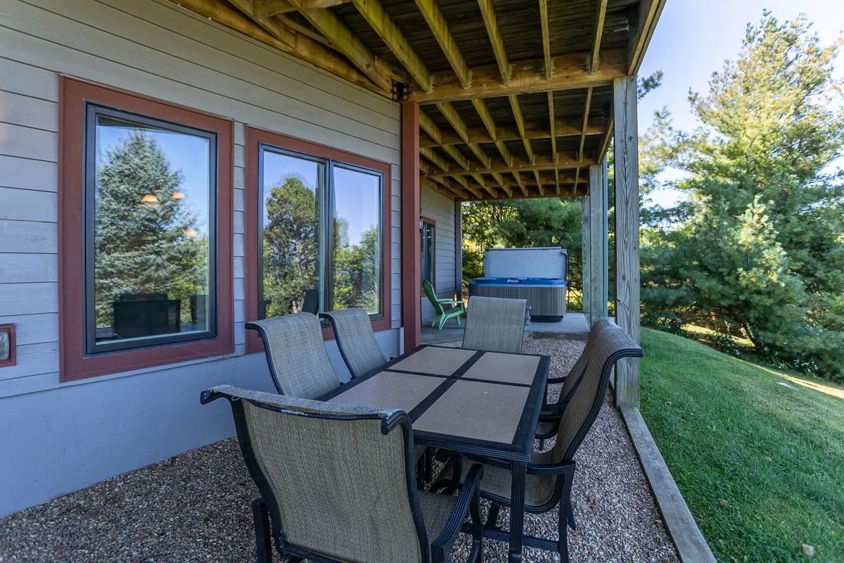 This exterior image showcases an inviting outdoor dining table and a hot tub set amid lush greenery. The patio offers ample space for group gatherings or meals under the sky, while the hot tub provides a relaxing spot with scenic mountain views that become even more magical at sunset or under the stars.