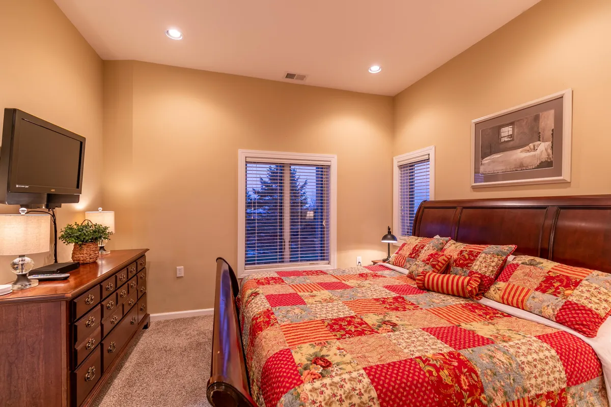 A comfortable bedroom with a cozy bed, TV, large window with a view, and a simple dresser. The soft lighting and thoughtful layout suggest a space perfect for relaxing, unwinding, or enjoying quiet evenings.