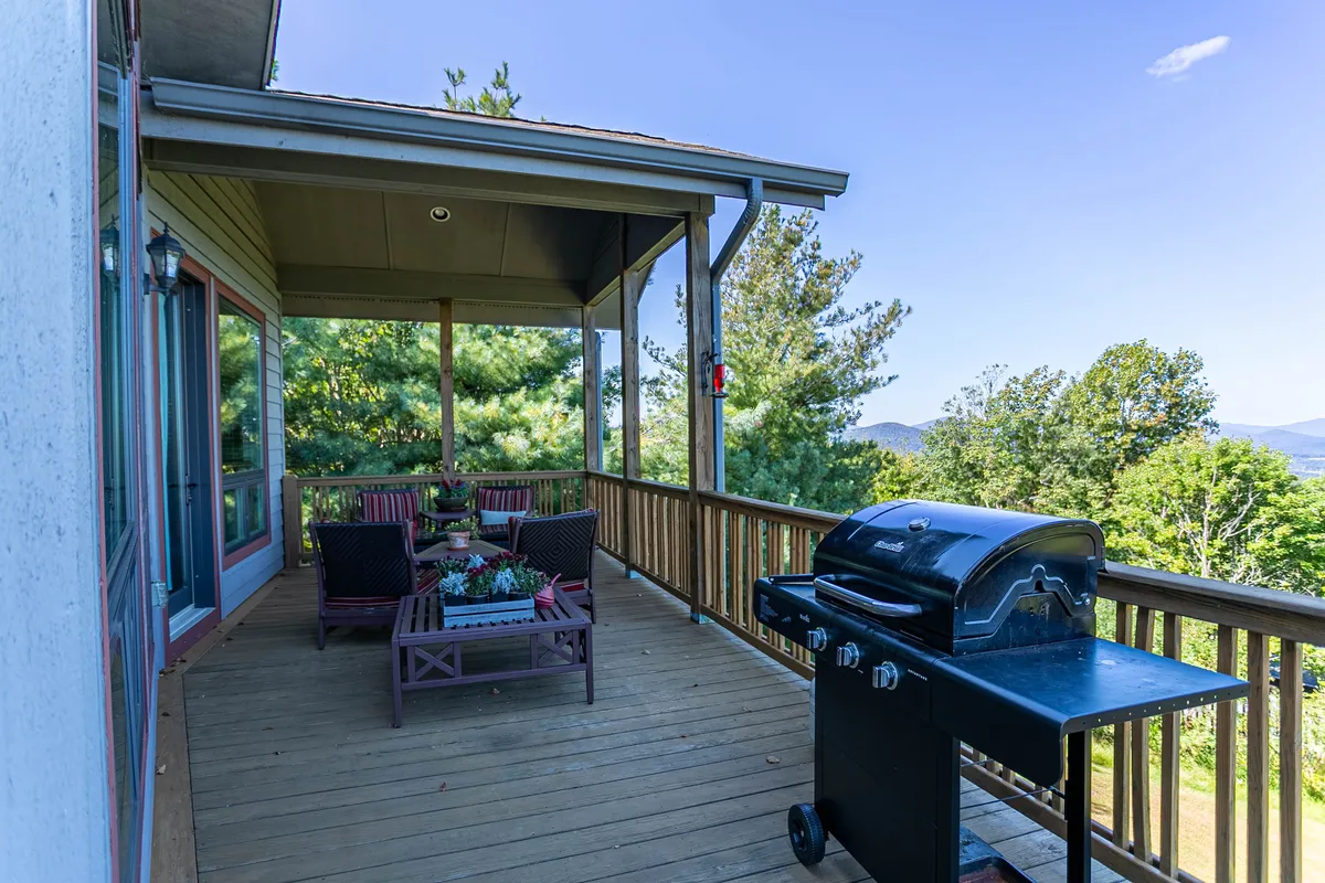 A cozy outdoor seating area featuring a grill and comfortable chairs, set against a backdrop of lush greenery and distant mountains. The space is perfect for barbecues, sunset watching, and enjoying the fresh alpine air with company—including pets.