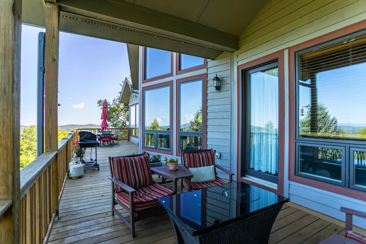 This exterior image showcases a spacious outdoor seating area with comfortable chairs, a grill, and expansive views of the surrounding landscape. Large windows connect the interior of the house to the outdoors, reinforcing the property's connection to nature and the neighborhood. The setting feels welcoming and perfect for relaxing after a pet-friendly walk or a day exploring local trails.
