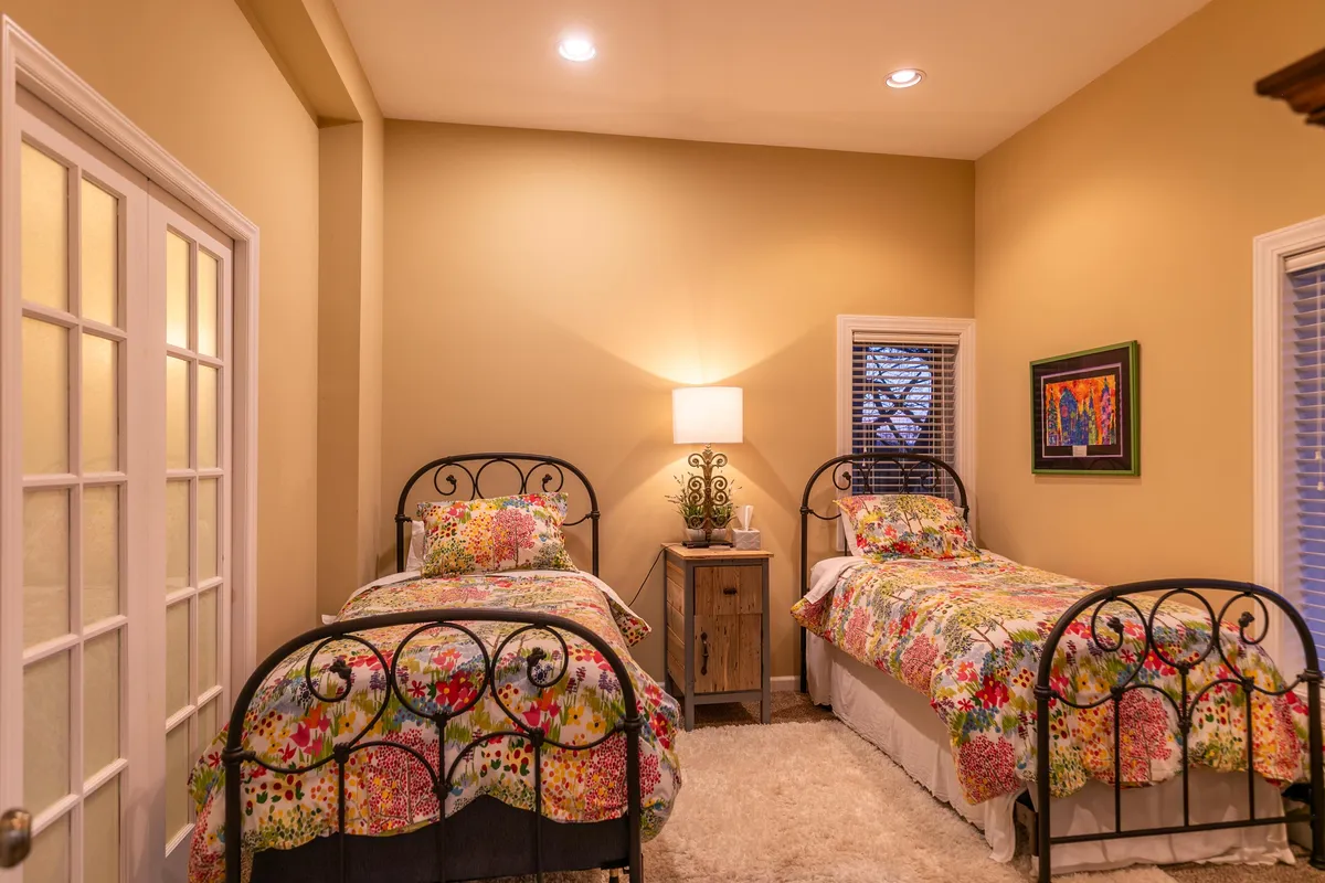A pair of twin beds with charming floral bedding and a decorative lamp on the nightstand, set against the backdrop of playful, colorful artwork. The intimate layout suggests a space suited for late-night conversations or comfortable family stays.