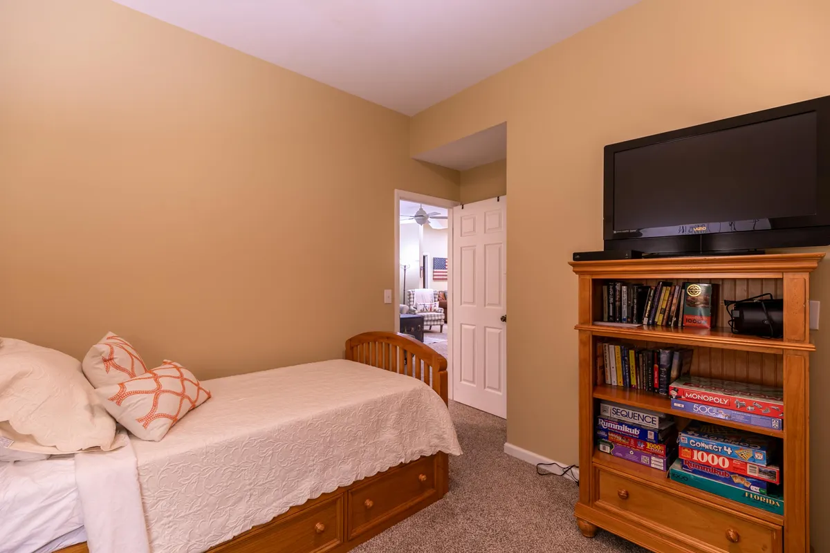 A welcoming space featuring a bed with decorative pillows, a wooden bookshelf, and a television. Board games are visible, suggesting a family-friendly zone perfect for game nights and quiet indoor entertainment.