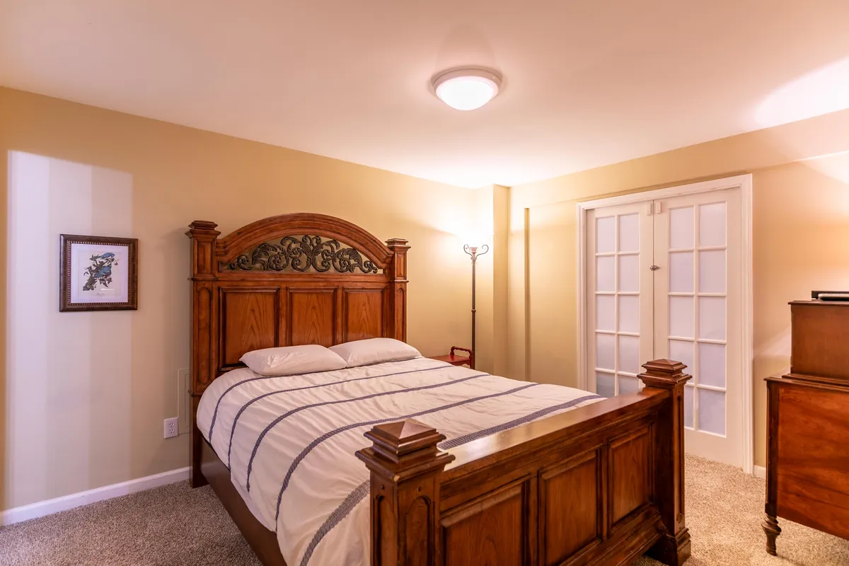 A warmly lit bedroom with a sturdy wooden bed frame, crisp white bedding, and tasteful artwork on the wall. Sunlight filters through windows, creating a peaceful and inviting atmosphere ideal for unwinding after a day of adventure.